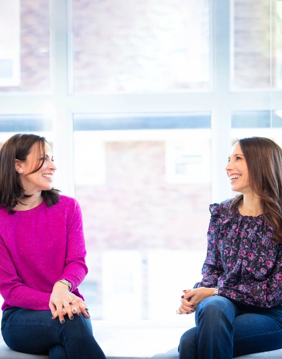 Dr. Jill Schwartz, in pink, and Dr. Dayna Zoller, the founding doctors of Summit Dental Partners, talking by a sunlit window.