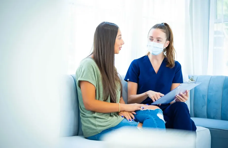A team member going through a form with a patient on the blue velvet sofa in the lounge.