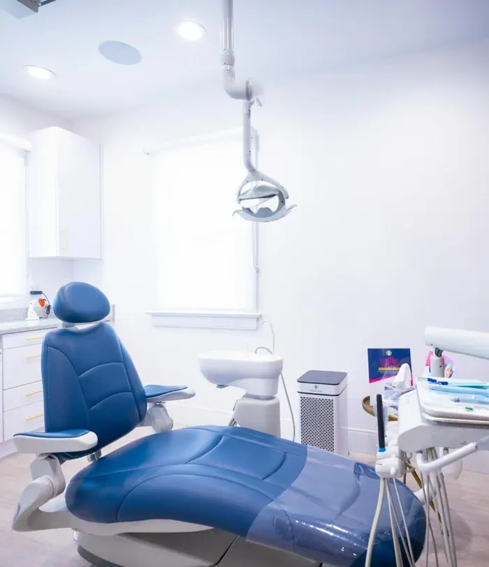 A treatment room with a blue dental chair and patterned navy wallpaper.